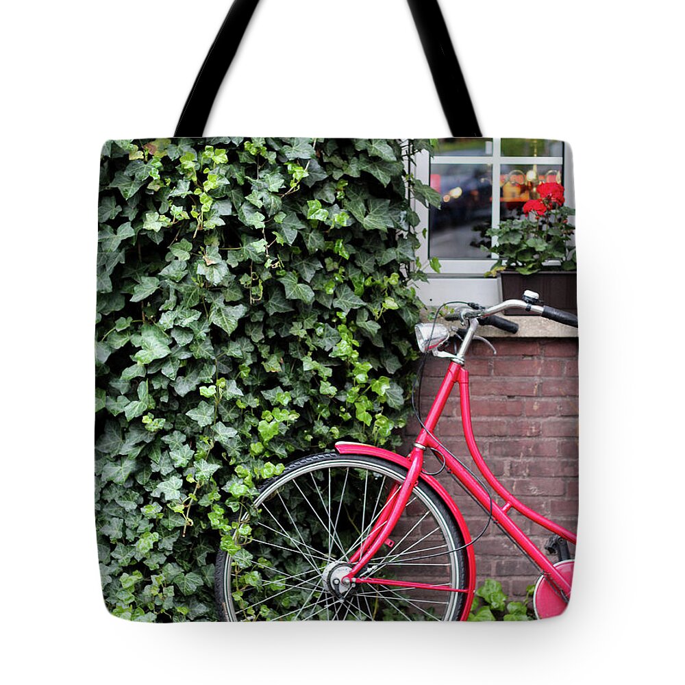 North Rhine Westphalia Tote Bag featuring the photograph A Red Bicycle Leaning Against A Wall by Carolin Voelker