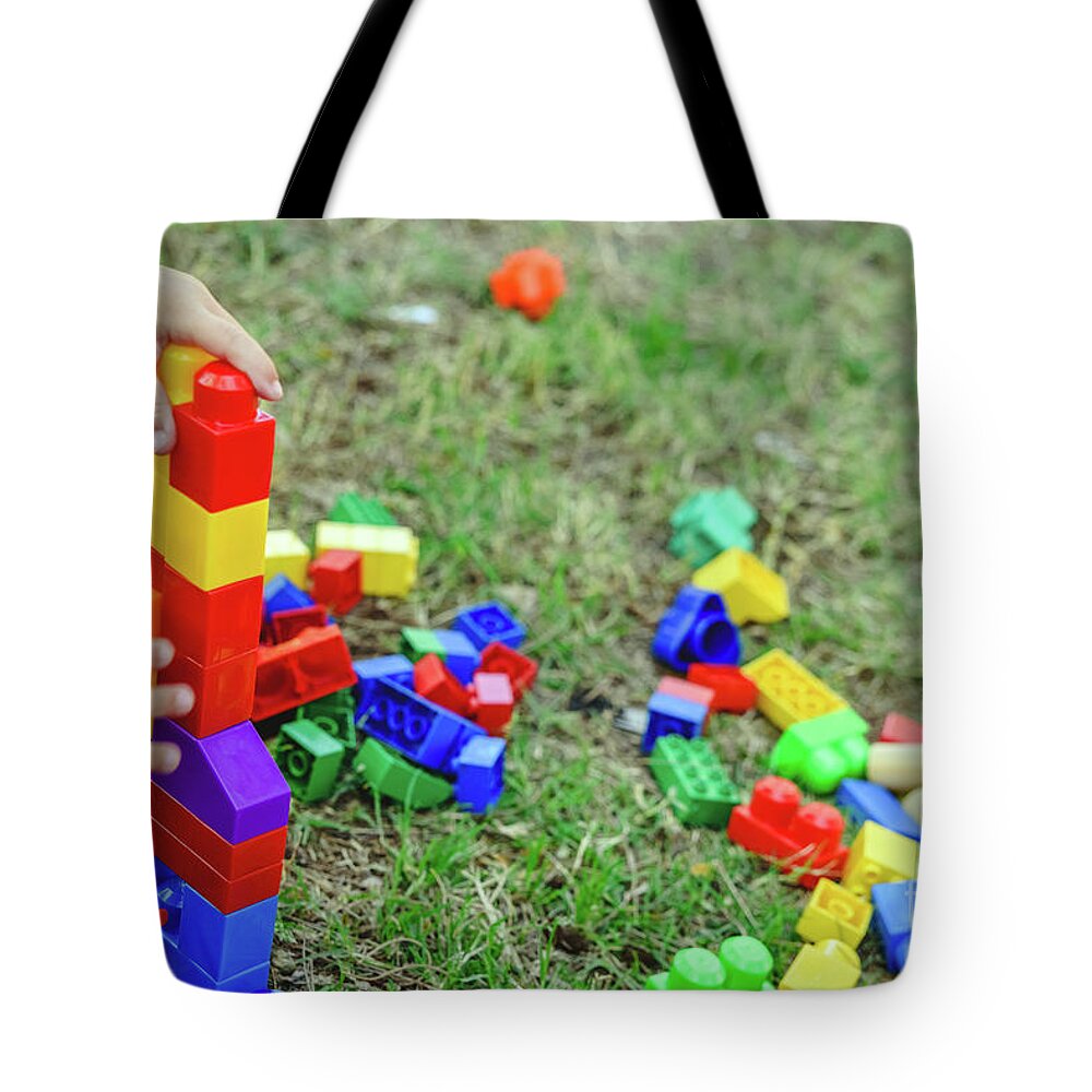 Activity Tote Bag featuring the photograph Child playing with colorful blocks sitting on the ground of a garden in spring, negative space. by Joaquin Corbalan