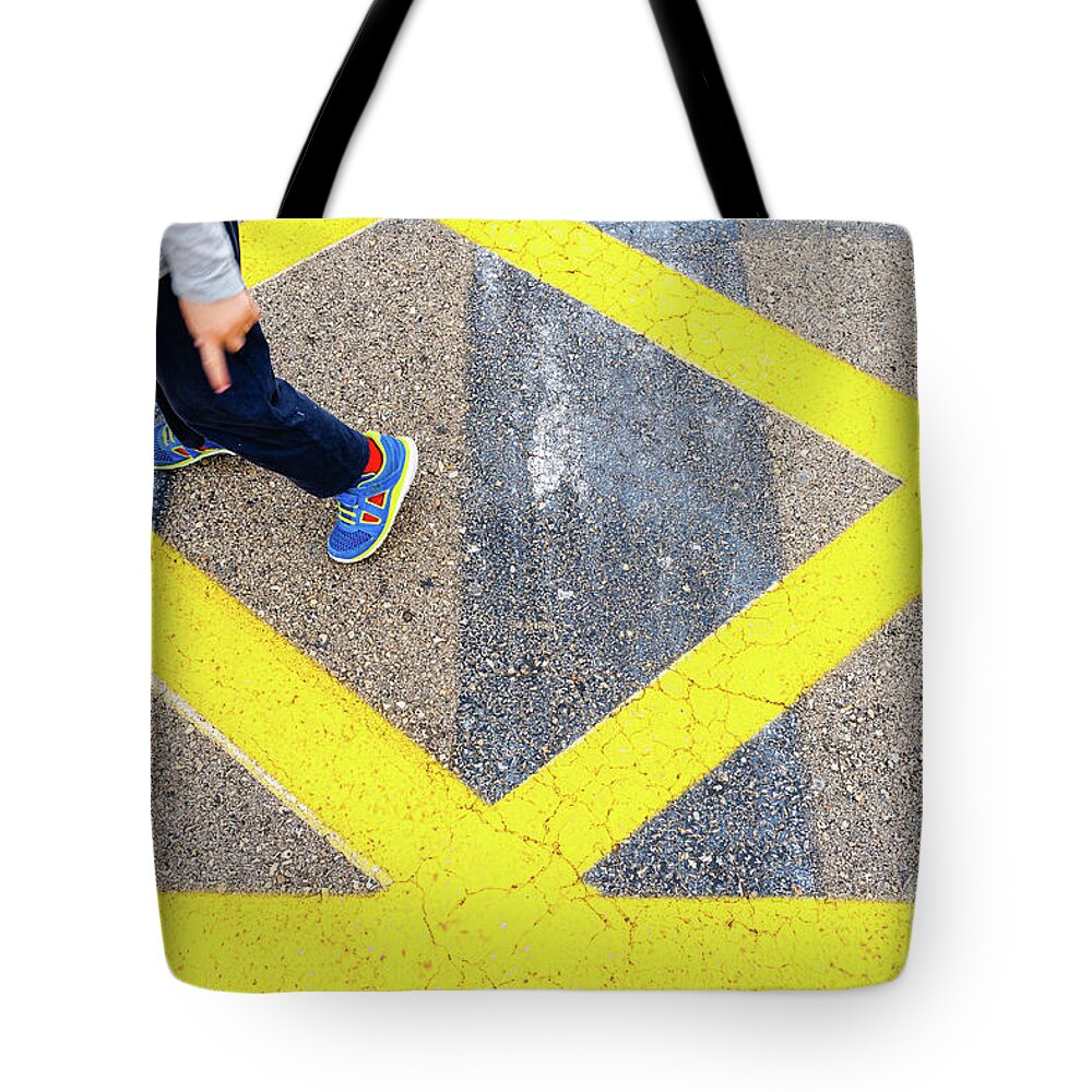 Asphalt Tote Bag featuring the photograph Child's legs on yellow lines on asphalt. by Joaquin Corbalan