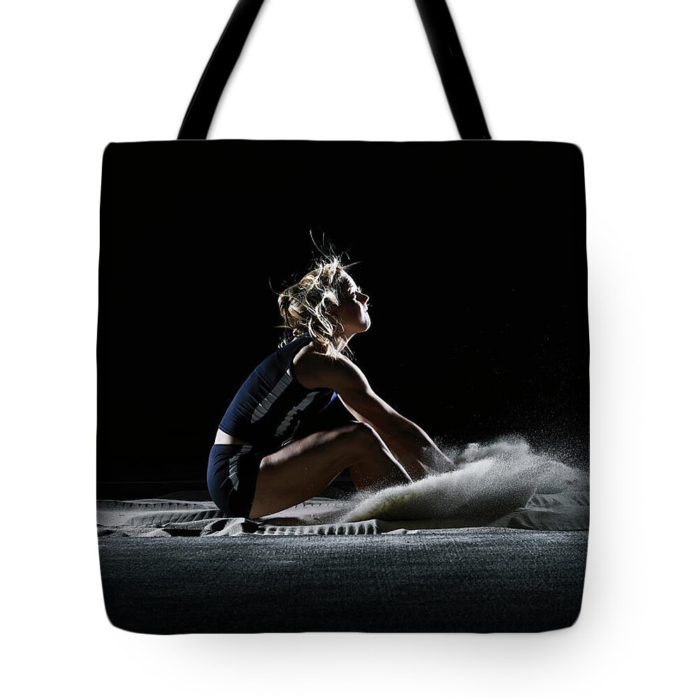 Three Quarter Length Tote Bag featuring the photograph Female Athlete Landing In Long Jump by Thomas Barwick
