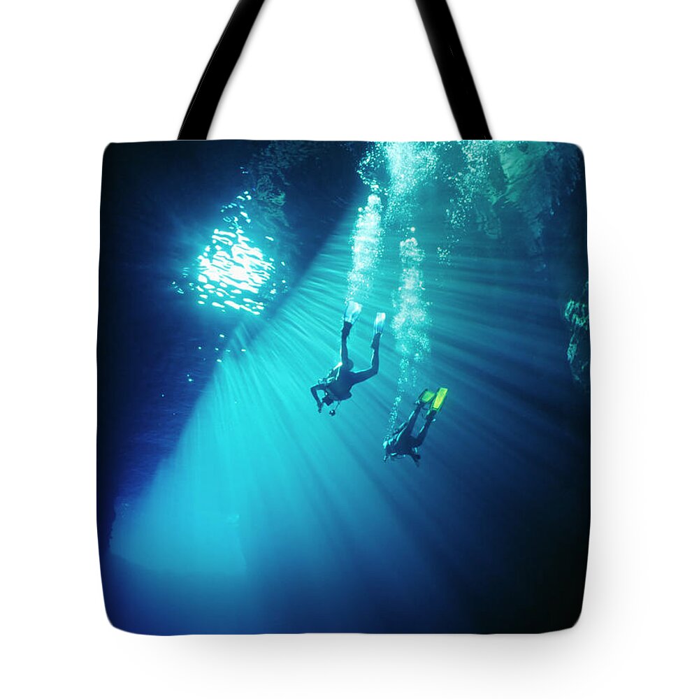 Underwater Tote Bag featuring the photograph Two Divers Swim Thru Sunbeams In Sea by Kim Westerskov