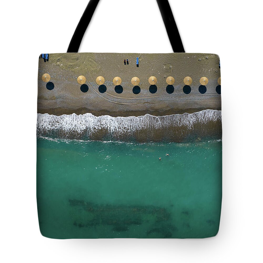  Beach Tote Bag featuring the photograph Aerial view from a flying drone of beach umbrellas in a row on a by Michalakis Ppalis