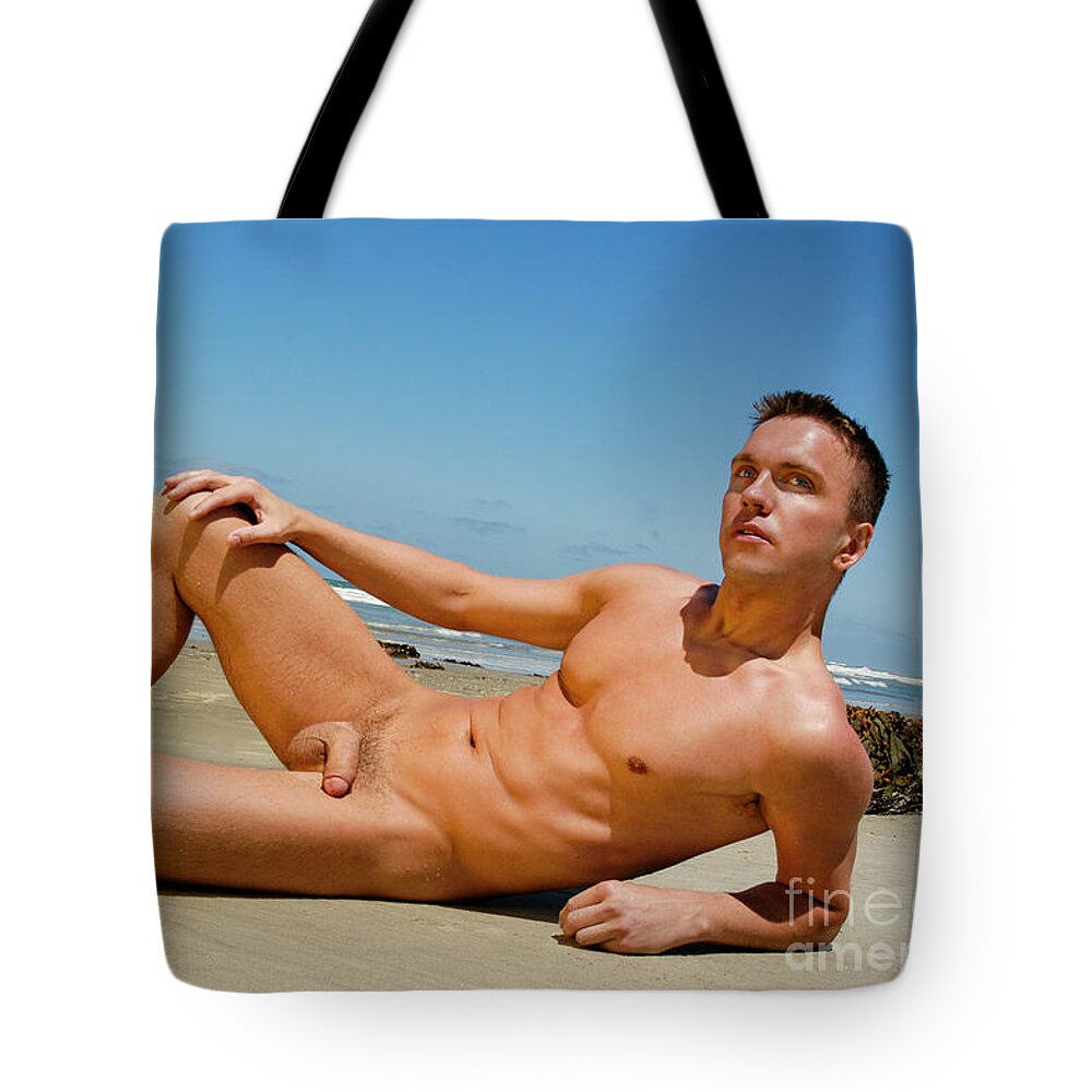 Nude Tote Bag featuring the photograph Handsome nude and muscular man poses on the wet sand at the beach. by Gunther Allen