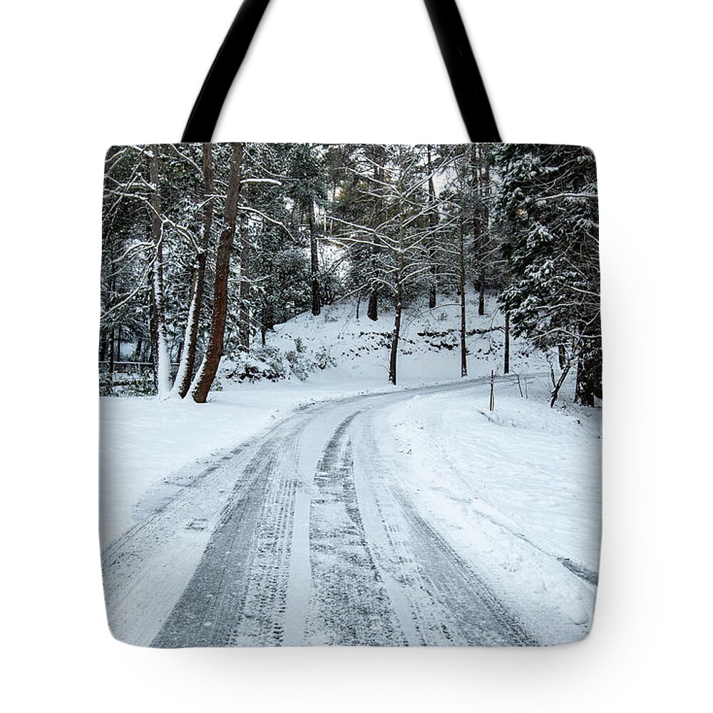 Frozen Road Tote Bag featuring the photograph Icy slippery dangerous road in winter in the forest. Snowy mountains snowstorm. by Michalakis Ppalis