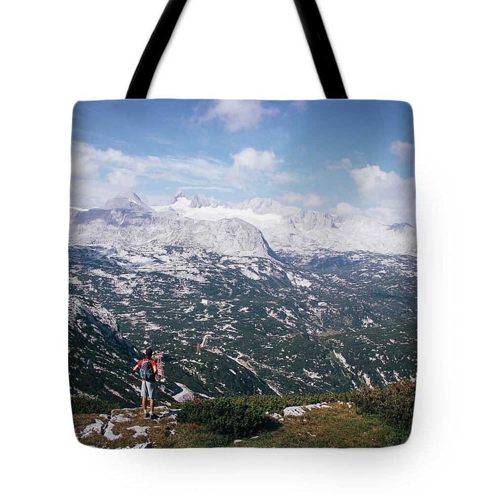 Sportive Tote Bag featuring the photograph Man with a backpack looks at the Dachstein massif by Vaclav Sonnek