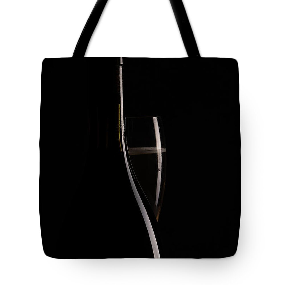 Red Wine Tote Bag featuring the photograph Red sparking wine on a wineglass and black wine bottle. by Michalakis Ppalis