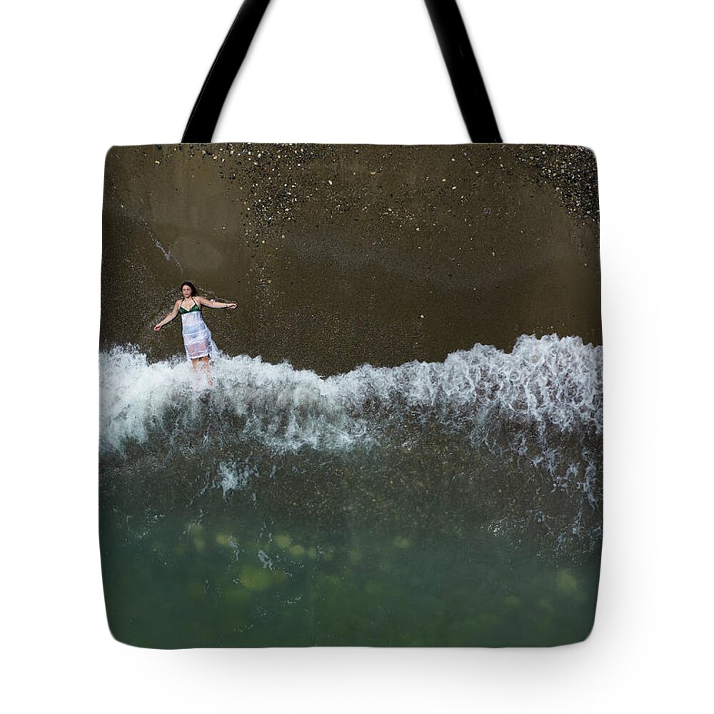 Holidays Tote Bag featuring the photograph Woman with white dress resting on a sandy beach with braking waves on the shore. Overhead shot. Aerial drone photograph by Michalakis Ppalis