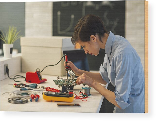 Expertise Wood Print featuring the photograph Woman Soldering a circuit board in her tech office. #1 by Vgajic