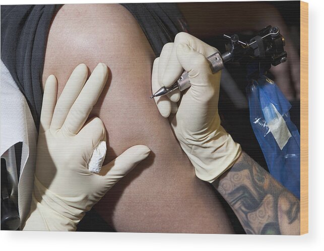 Expertise Wood Print featuring the photograph A tattoo artist preparing to tattoo a man's bare arm, close-up by Halfdark