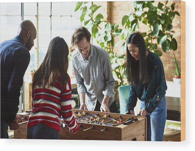 Cool Attitude Wood Print featuring the photograph Four friends playing foosball and laughing in modern apartment by 10'000 Hours
