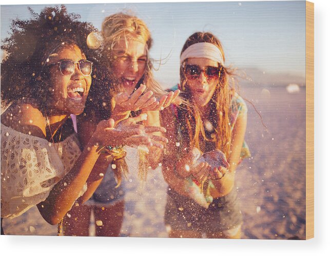 Adolescence Wood Print featuring the photograph Girls blowing confetti from their hands on a beach by Wundervisuals