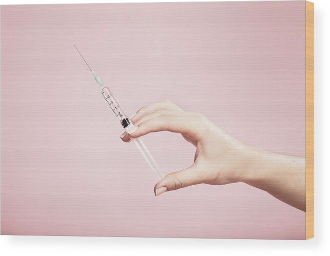 People Wood Print featuring the photograph Hand holding syringe in plain pink background by Paper Boat Creative