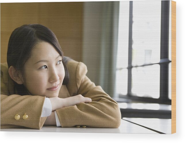 Human Arm Wood Print featuring the photograph Teenage girl sitting and leaning on desk in classroom, smiling and looking away by Daj