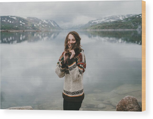 Tranquility Wood Print featuring the photograph Woman in knitted sweater laughing near the fjord in Norway by Oleh_Slobodeniuk