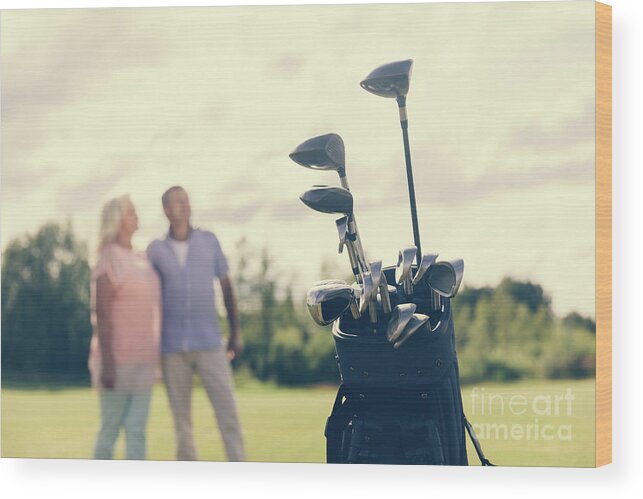 Golf Wood Print featuring the photograph Golf bag standing on a grass field, people in the background by Michal Bednarek