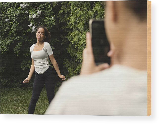 Sibling Wood Print featuring the photograph Mixed-race teenage sisters filming with mobile phone in backyard. #1 by Martinedoucet