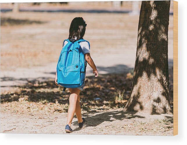 4-5 Years Wood Print featuring the photograph A black-haired girl with a blue backpack, turned her back, walks through a park in the direction of school. Concept of education and back to school. by DBenitostock