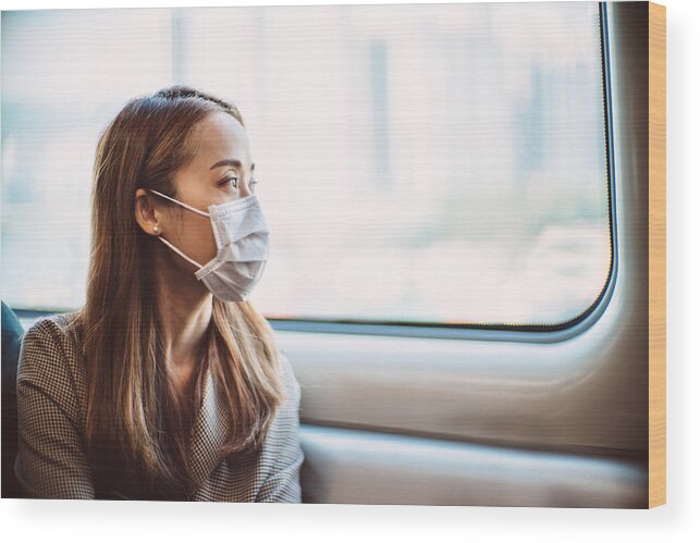 Air Pollution Wood Print featuring the photograph Businesswoman with protective face mask looking out of the window of train in thought by Images By Tang Ming Tung