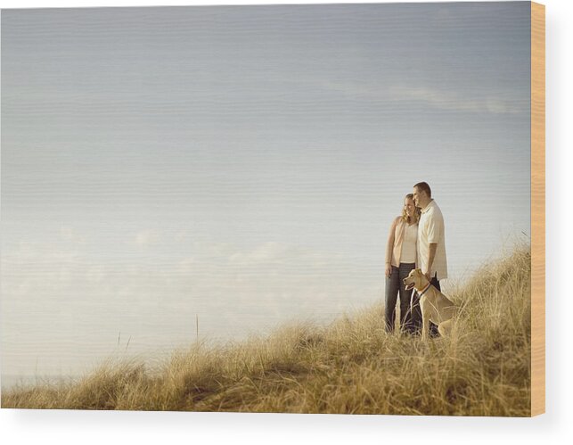 Tranquility Wood Print featuring the photograph Caucasian couple walking dog on grassy dunes by Chris Clor