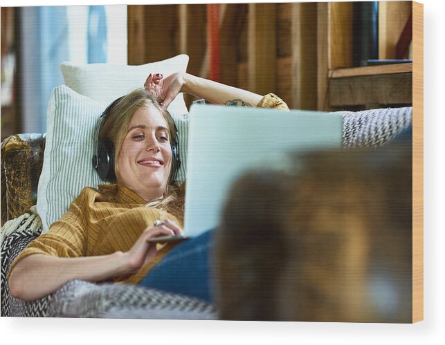 Tranquility Wood Print featuring the photograph Cheerful mid adult woman using laptop and smiling with headphones by 10'000 Hours