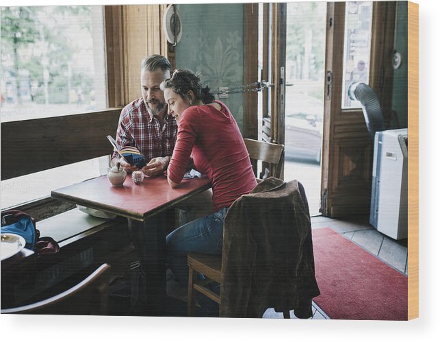 Heterosexual Couple Wood Print featuring the photograph Couple in Cafe reading Tour Guide by Hinterhaus Productions