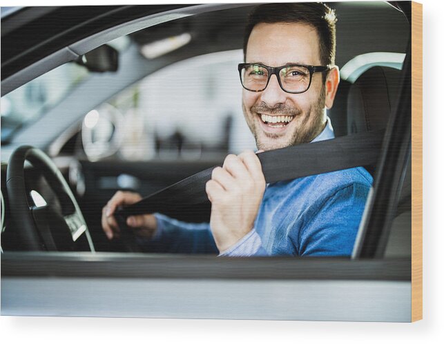 Young Men Wood Print featuring the photograph Happy businessman fastening seatbelt before his trip by car. by Skynesher