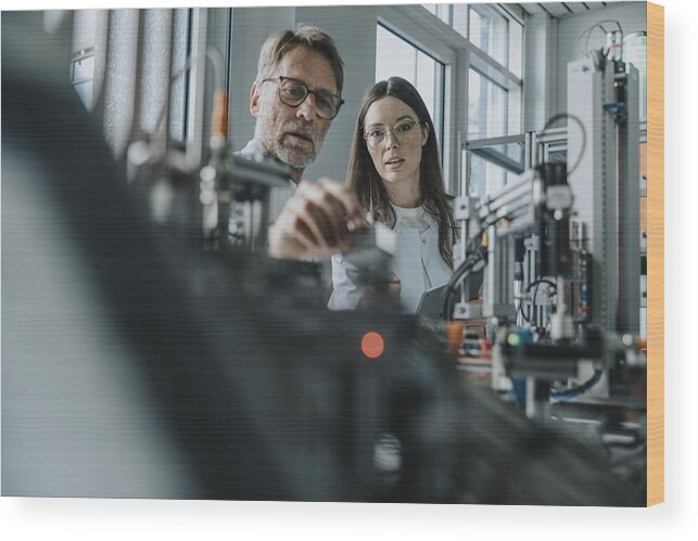 Expertise Wood Print featuring the photograph Male scientist with young woman examining machinery in laboratory by Westend61