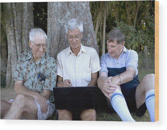 Three Quarter Length Wood Print featuring the photograph Mature man and senior men by tree, looking at laptop screen, smiling by Manchan