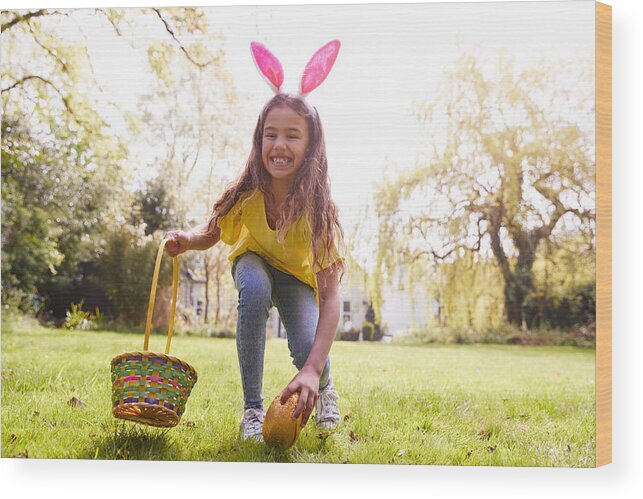 Easter Wood Print featuring the photograph Portrait Of Girl Wearing Bunny Ears Finding Chocolate Egg On Easter Egg Hunt In Garden by Monkeybusinessimages