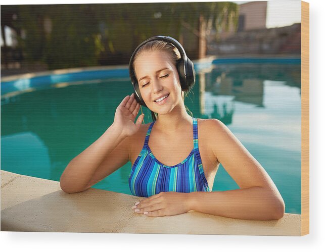 People Wood Print featuring the photograph Relaxed smiling woman listening to music in headphones bathing in swimming pool. Blonde girl enjoys favourite song with goosebumps on skin. Waterproof headphones with touch control mobility concept by Artiemedvedev