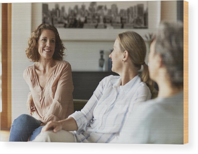 Three Quarter Length Wood Print featuring the photograph Woman conversing with friends at home by Morsa Images