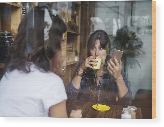 Accessibility Wood Print featuring the photograph Woman with friend in a cafe holding smartphone and drinking coffee by Westend61