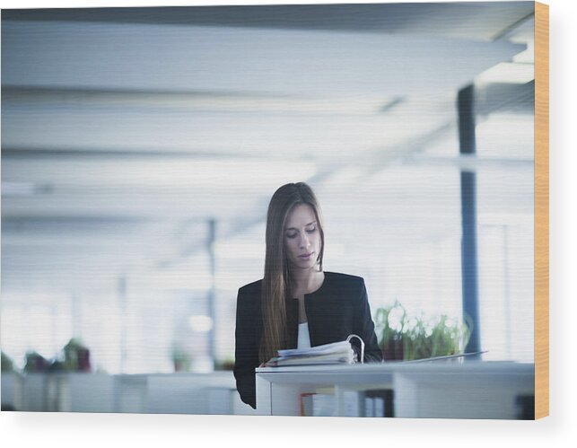 Working Wood Print featuring the photograph Young woman in office looking down at paperwork in ringbinder file by Sigrid Gombert
