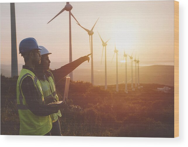 Young Men Wood Print featuring the photograph Young maintenance engineer team working in wind turbine farm at sunset #1 by Serts