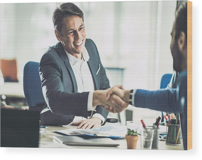 Working Wood Print featuring the photograph Happy mid adult insurance agent shaking hands with his customer in the office. by Skynesher