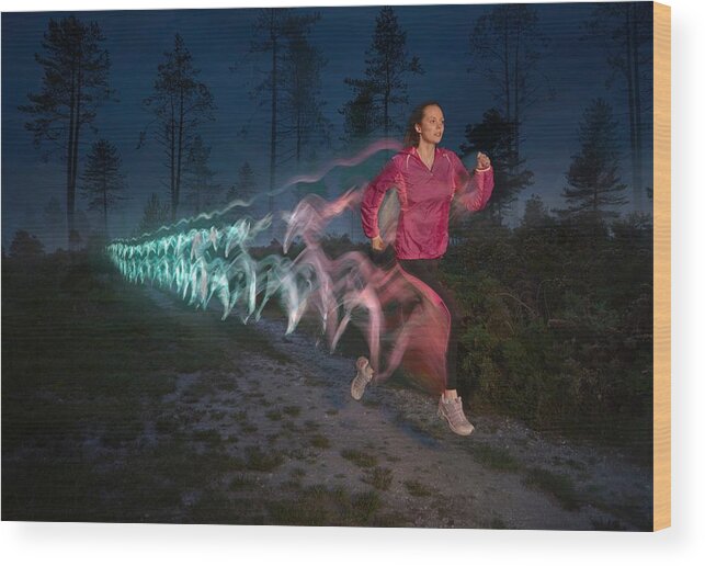 Following Wood Print featuring the photograph Young woman followed by light trails running on forest dirt track at night by Cultura RM Exclusive/J J D