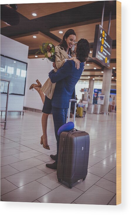 Young Men Wood Print featuring the photograph Excited young man welcoming girlfriend with flowers at airport by Wundervisuals