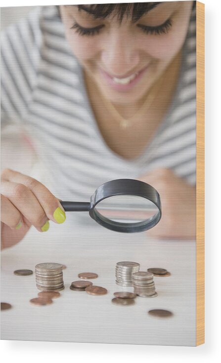 Coin Wood Print featuring the photograph Mixed race woman examining stacks of coins with magnifying glass by JGI/Jamie Grill