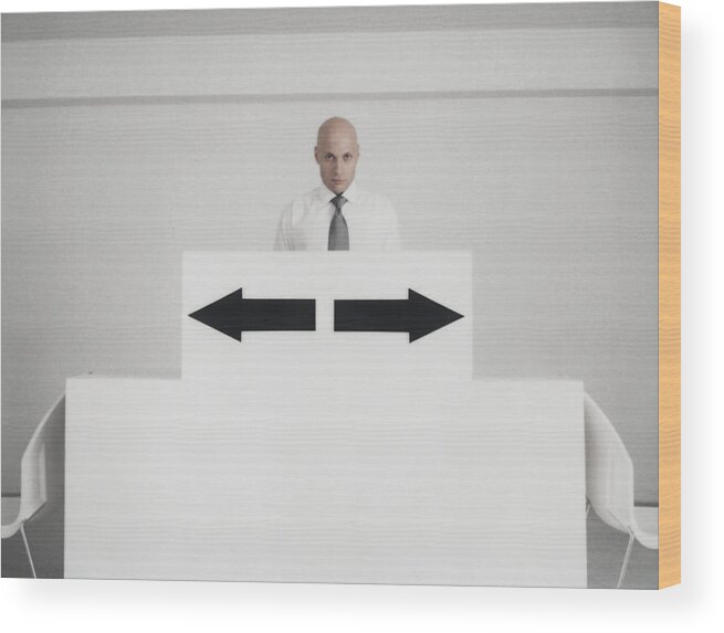 Corporate Business Wood Print featuring the photograph Man standing behind podium with two arrow signs pointing in opposite directions by Matthieu Spohn