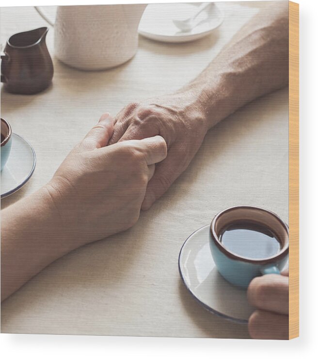 Breakfast Wood Print featuring the photograph Cropped image of senior couple holding hands and drinking coffee by Istetiana