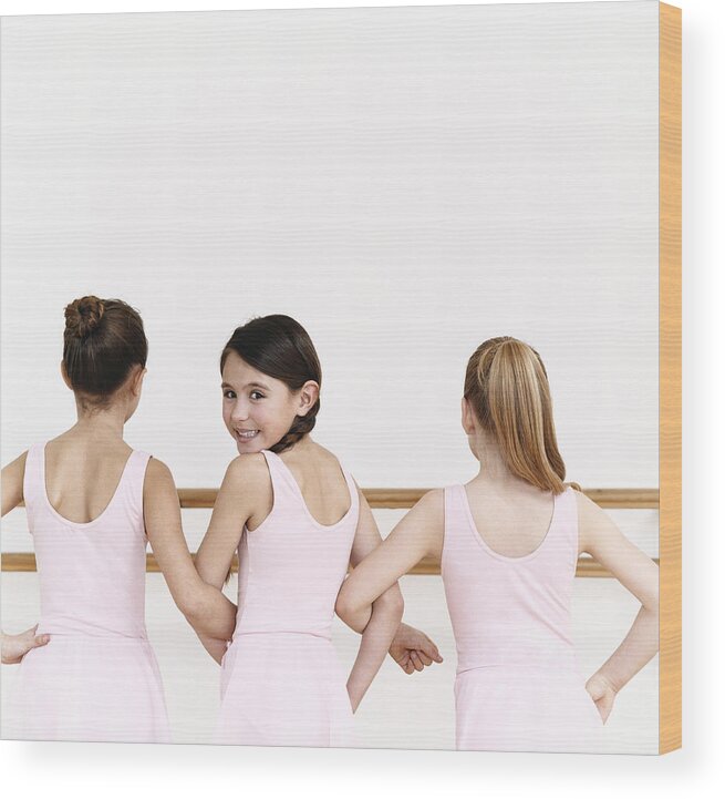 Ballet Dancer Wood Print featuring the photograph Rear View of a Line of Young, Female Ballet Dancer Practicing in the Dance Studio With One Ballerina Looking Behind Her by Digital Vision.