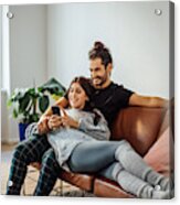 Young couple with mobile phone relaxing on sofa Acrylic Print