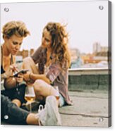 Woman Showing Mobile Phone To Friend While Sitting On Terrace During Rooftop Party Acrylic Print