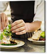 Close Up Of Chef In Kitchen Adding Salad Garnish To A Plate With Grilled Fish. Canvas Print