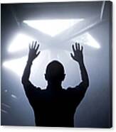Silhouette Of A Man With Raised Hands Against Light Coming From Above. Canvas Print