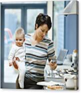 Woman Stands By A Kitchen Counter Holding Her Baby And Dialing Her Mobile Phone Canvas Print