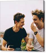 Happy Man Showing Mobile Phone To Friend Having Drink At Terrace During Party Canvas Print