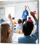 Rear View Of Students Sitting With Hands Raised In Classroom Canvas Print