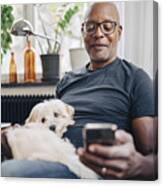 Smiling Retired Senior Male Using Smart Phone While Sitting With Dog In Room At Home Canvas Print