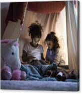 Two Sisters Sitting In Dark Children's Room, Looking At Digital Tablet Canvas Print